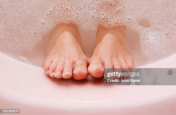 woman's feet resting against bath tub with bubbles - female feet stock-fotos und bilder