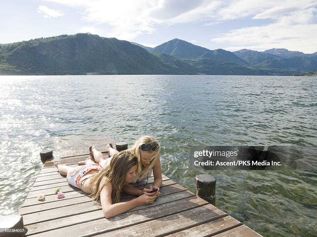 Mother & daughter text message on wooden lake pier