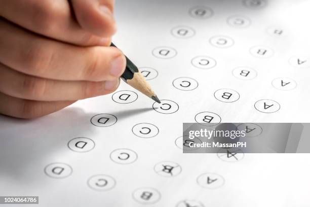 child's hand filling in a multi-answer test with a pencil - marked sheet of paper imagens e fotografias de stock