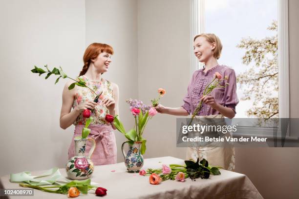 2 women laughing while arranging flowers. - floral arranging stock pictures, royalty-free photos & images