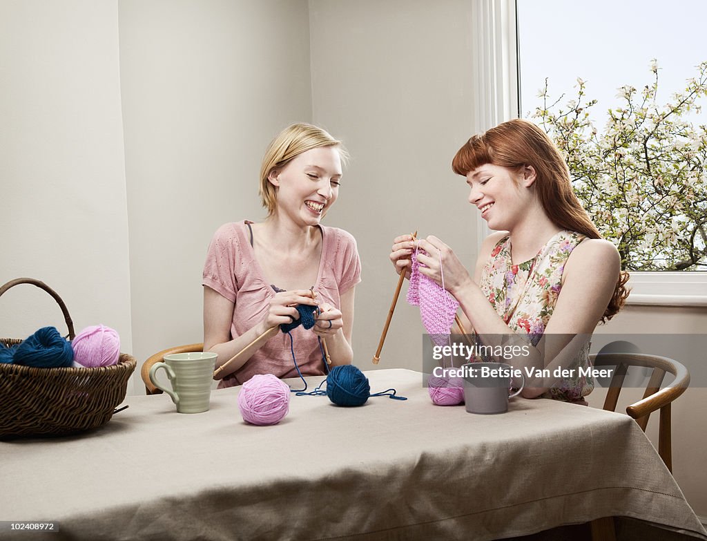 Two women knitting at table.