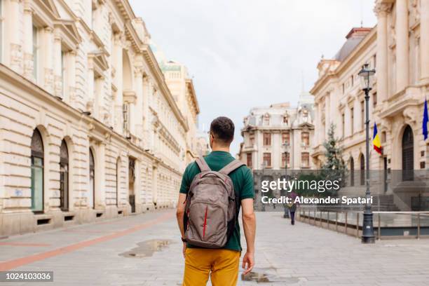 rear view of a young man with backpack walking on the street in the old town of bucharest - bucharest stock pictures, royalty-free photos & images
