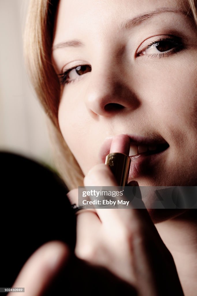 Portrait of young woman, applying lipstick