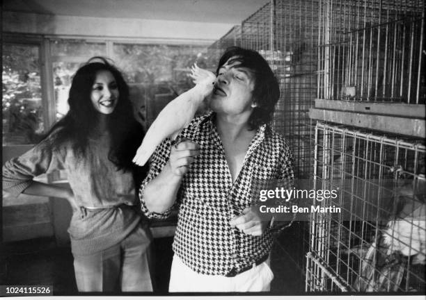 English photographer David Bailey kissing parrot with fashion model Marie Helvey, London, UK, August 8 1977.