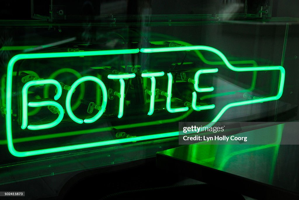 Green neon sign shaped as bottle in window of bar.
