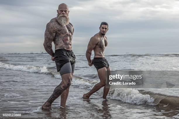 getatoeëerde senior man jongeman tijdens training coaching - muscle men at beach stockfoto's en -beelden