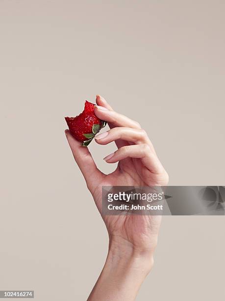 woman holding strawberry with a bite taken out - beige background stock pictures, royalty-free photos & images
