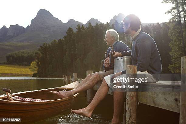 father and son having a beer on jetty - family smile stock-fotos und bilder