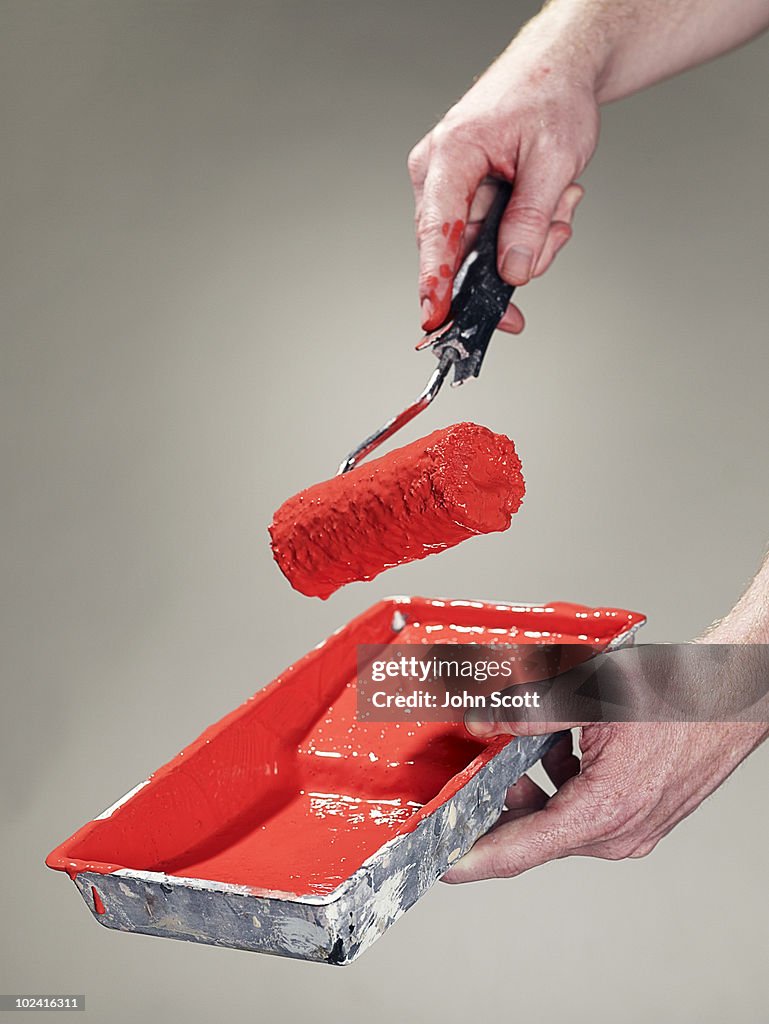 Hand holding a paint roller and tray of paint