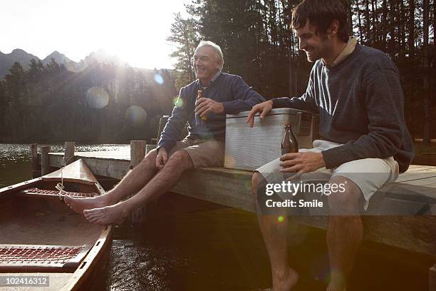 father and son having a beer on jetty - friends smile stock-fotos und bilder