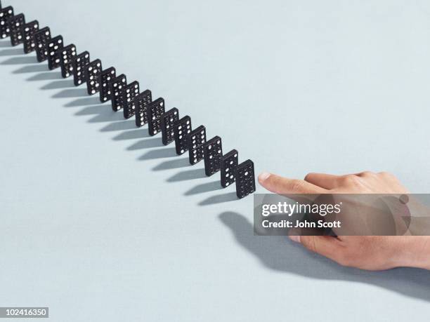 man pointing at a row of dominoes - dominoeffekt stock-fotos und bilder