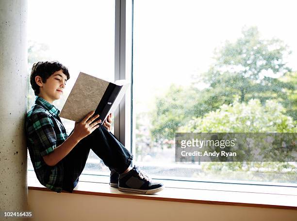 boy reading book sitting in window nook - boy reading a book stock-fotos und bilder