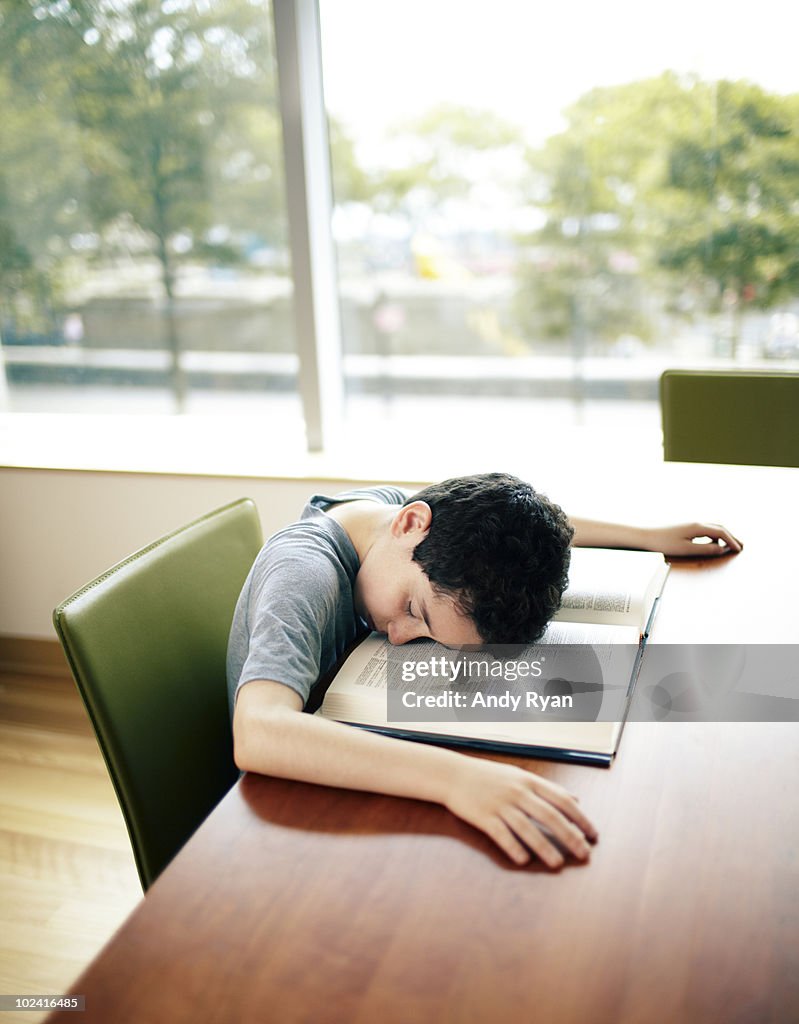 Boy asleep facedown in book at library