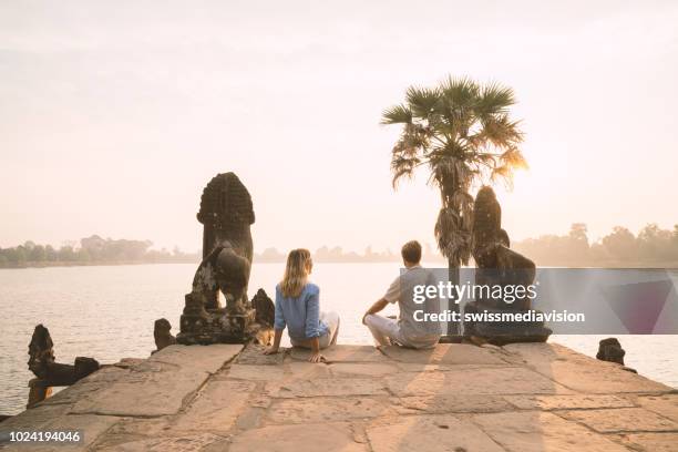 jovem casal contemplando o antigo templo à beira do lago no camboja, nascer do sol, as pessoas viajam conceito de romance casal descoberta - angkor wat - fotografias e filmes do acervo