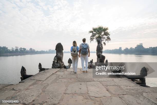 young couple contemplating ancient temple by the lake in cambodia , sunrise, people travel discovery couple romance concept - angkor wat stock pictures, royalty-free photos & images