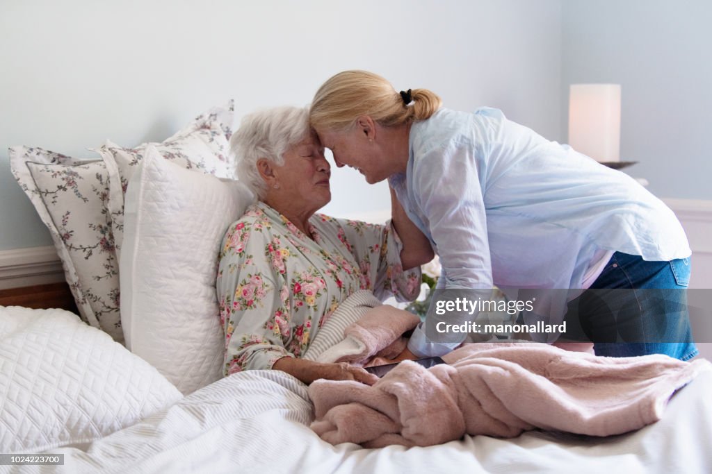 Une femme senior dans son lit, embrassant sa fille avec émotion