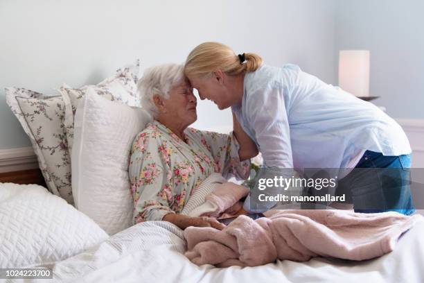 a senior woman in her bed embracing her daughter with emotion - end of life care stock pictures, royalty-free photos & images