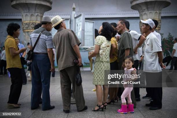 Little girl looks back away as people read a newspaper displayed in a station on the Pyongyang metro on August 21, 2018 in Pyongyang, North Korea....