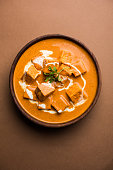Paneer Butter Masala also known as Panir  makhani or makhanwala. served in a ceramic or wooden bowl with fresh cream and coriander. Isolated over colourful moody background. selective focus