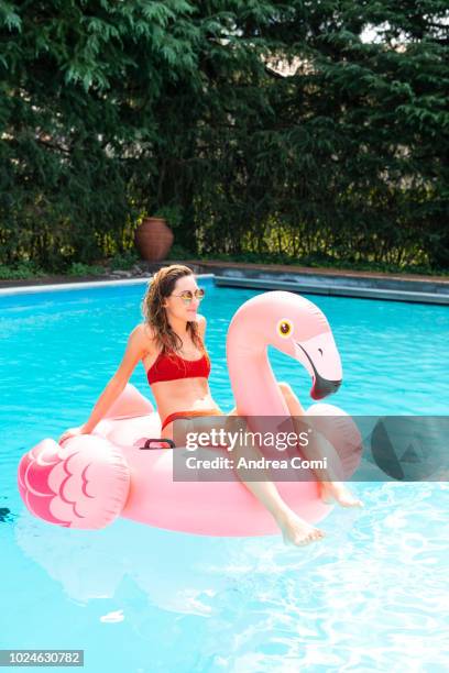 happy young woman with pink flamingo float in swimming pool - float imagens e fotografias de stock