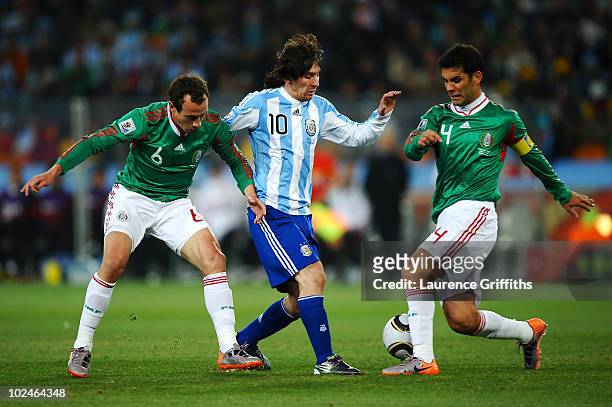 Lionel Messi of Argentina is tackled by Gerardo Torrado and Rafael Marquez of Mexico during the 2010 FIFA World Cup South Africa Round of Sixteen...