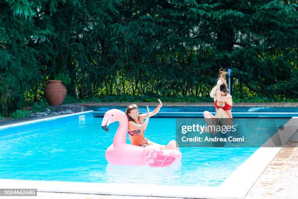 young woman jumping into a swimming pool with a friend on a flamingo float - woman free diving stock pictures, royalty-free photos & images