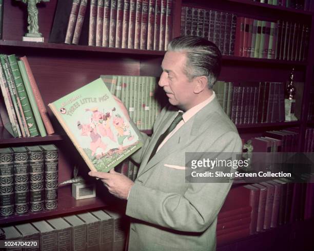 American film producer Walt Disney holding a Mickey Mouse Club edition of the 'Three Little Pigs' story, circa 1955.