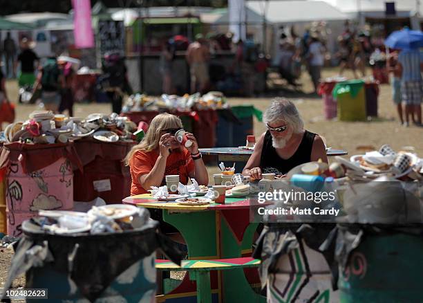 Couple eat breakfast while seated at a table surrounded with overflowing litter bins as festival-goers leave the 40th Glastonbury Festival at Worthy...