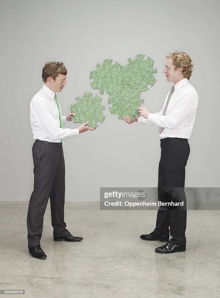Businessmen piecing a green puzzle together