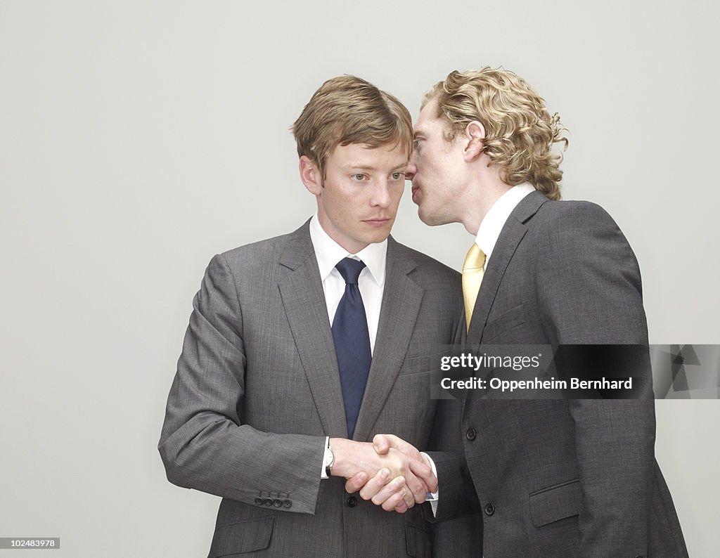 Businessmen whispering and shaking hands