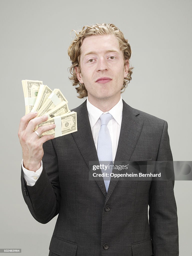 Businessman in suit fanning himself with money