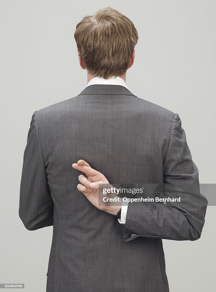 Man in suit with fingers crossed behind back