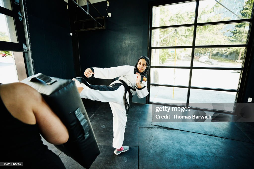 Female Muslim self defense instructor demonstrating kick during class in gym