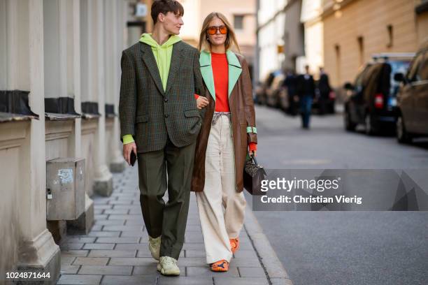 Guest wearing hoody, suit and a guest wearing brown leather coat, wide leg pants is seen during Stockholm Runway SS19 on August 28, 2018 in...