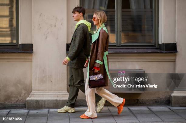 Guest wearing hoody, suit and a guest wearing brown leather coat, wide leg pants is seen during Stockholm Runway SS19 on August 28, 2018 in...