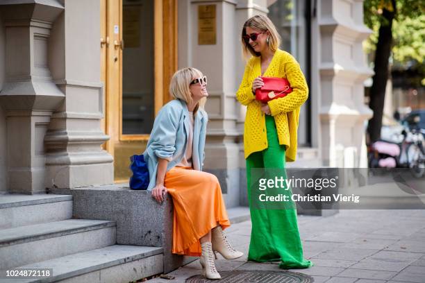Emili Sindlev wearing yellow knit cardigan, green wide leg pants, Burberry clutch and Jeannette Madsen wearing orange midi skirt, ankle boots, light...