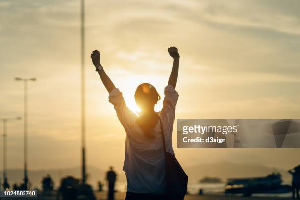young woman relaxing with hands in the air by the pier and enjoying the beautiful sunset and warmth of sunlight - emotional stress stock-fotos und bilder