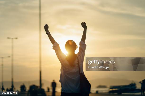 young woman relaxing with hands in the air by the pier and enjoying the beautiful sunset and warmth of sunlight - relief foto e immagini stock