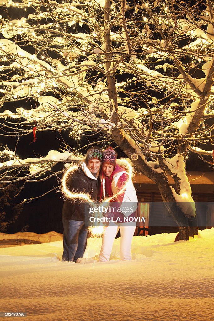 Young couple making heart shape with sparkler by night