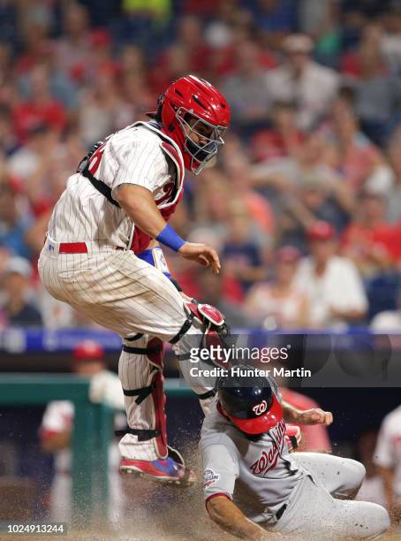 Jorge Alfaro of the Philadelphia Phillies leaps up to catch an errant throw as Anthony Rendon of the Washington Nationals slides safely into home...