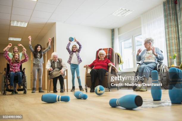 girls playing bowling with senior women in rest home - rentnersiedlung stock-fotos und bilder