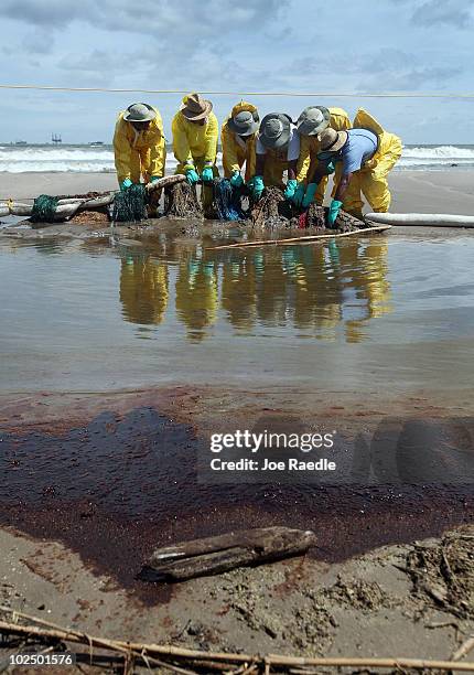 Crude oil lays on the ground in the foreground as workers are seen moving absorbent material as they try to capture some of the oil washing on to...