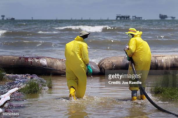 Workers are seen as they use a vacuum hose to capture some of the oil washing on to Fourchon Beach from the Deepwater Horizon oil spill in the Gulf...