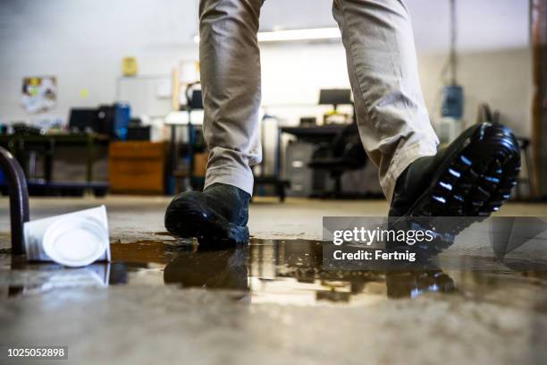 ein arbeiter in einem lagerhaus wandern in verschüttete flüssigkeit. - hazardous workplace stock-fotos und bilder