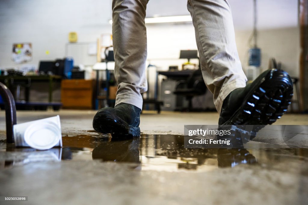Un operaio in un magazzino che cammina nel liquido versato.