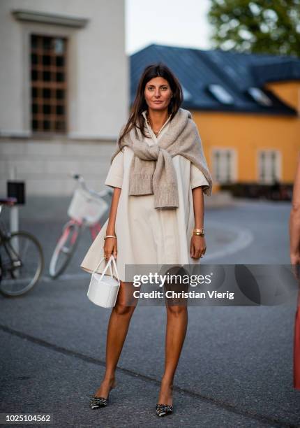 Giovanna Battaglia Engelbert wearing creme white dress, white bag, knit over her shoulders seen during Stockholm Runway SS19 on August 29, 2018 in...