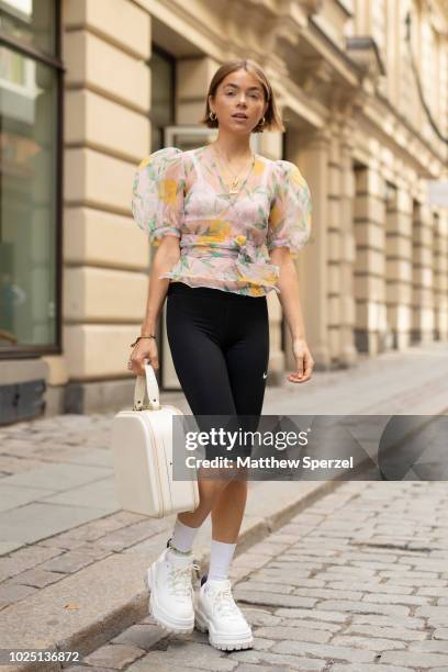 Guest is seen on the street during Fashion Week Stockholm SS19 wearing sheer floral top with spandex black shorts, white sneakers, and vintage...