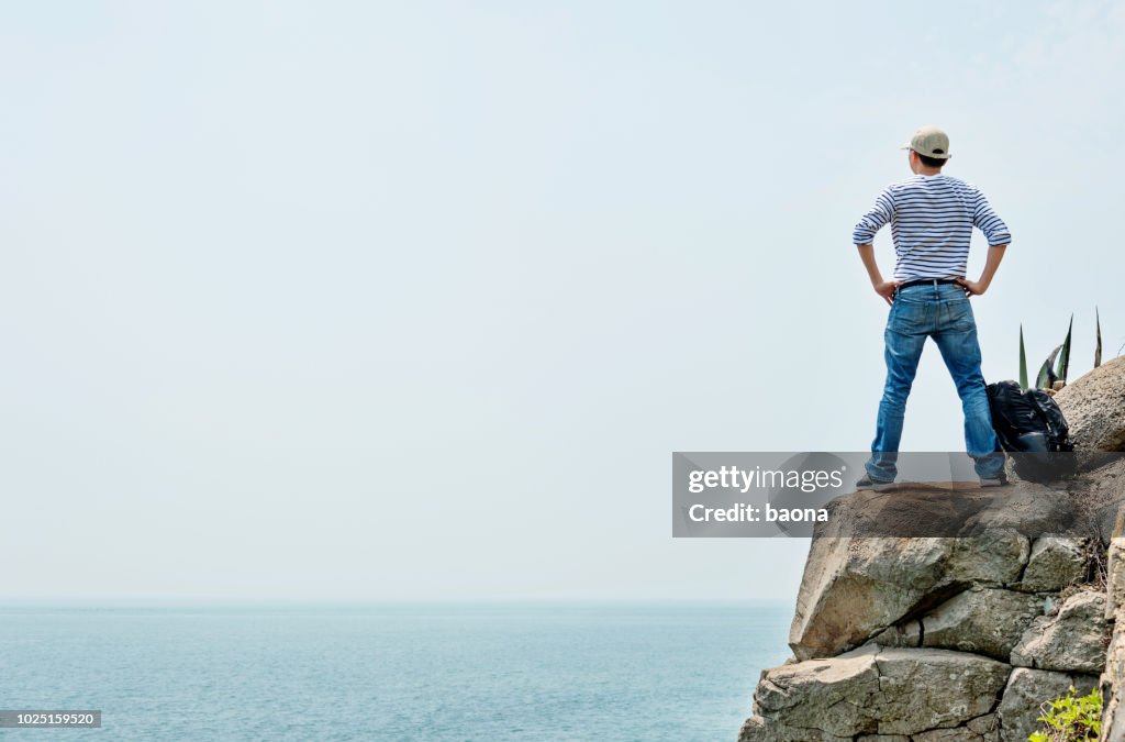 Man backpacker standing on the cliff by sea