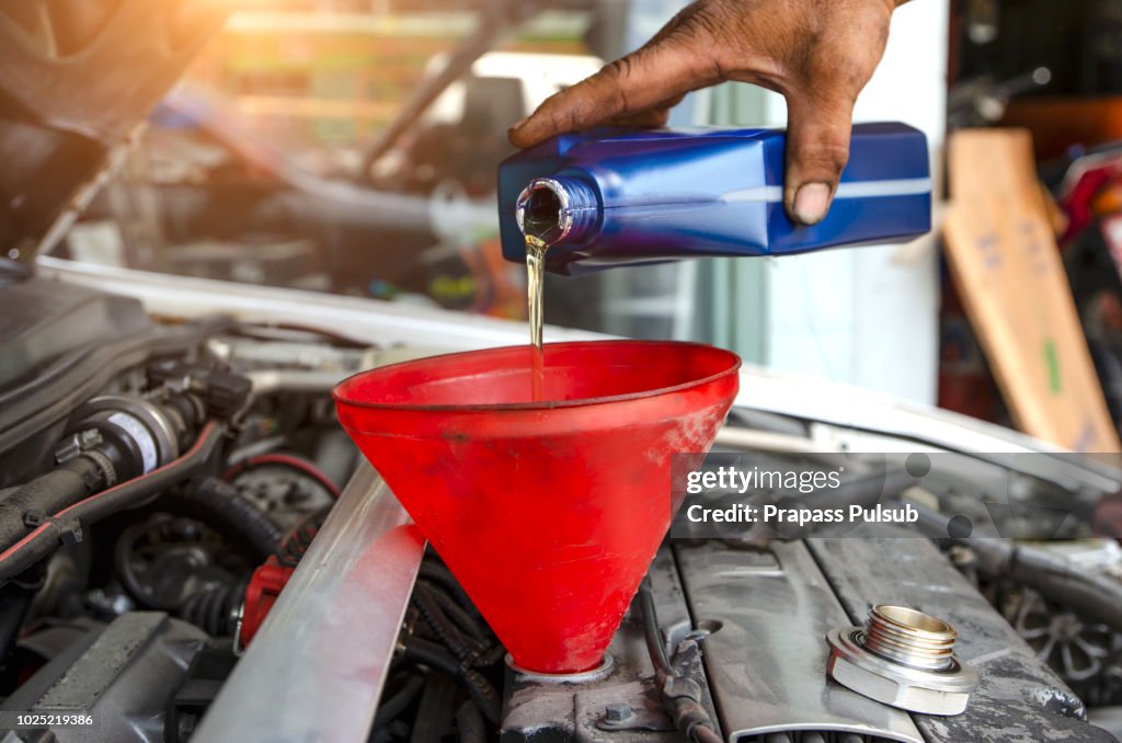 Car mechanic replacing and pouring fresh oil into engine at maintenance repair service station