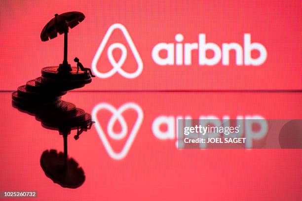 This illustration picture taken in Paris on August 29 a toy umbella and a figurine on coins next to the logo of rental website Airbnb.